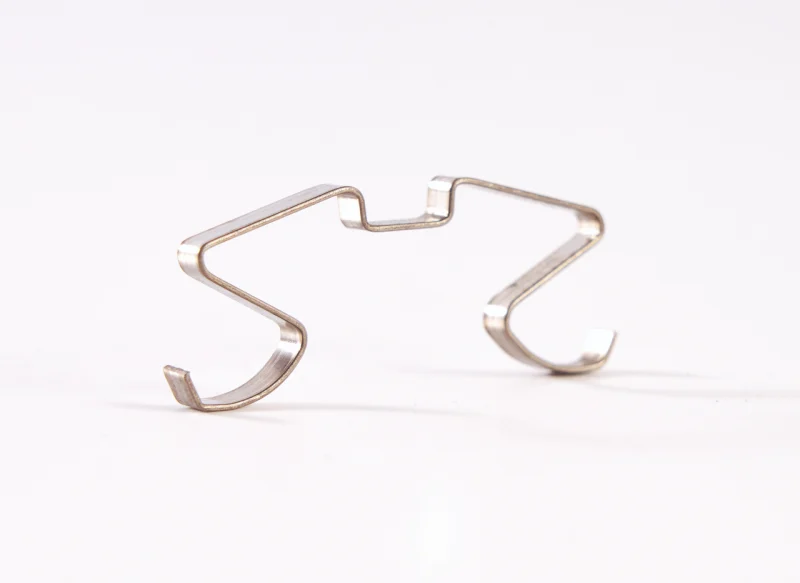 Pieza metálica de fleje de acero conformado con diseño simétrico de precisión sobre fondo blanco.