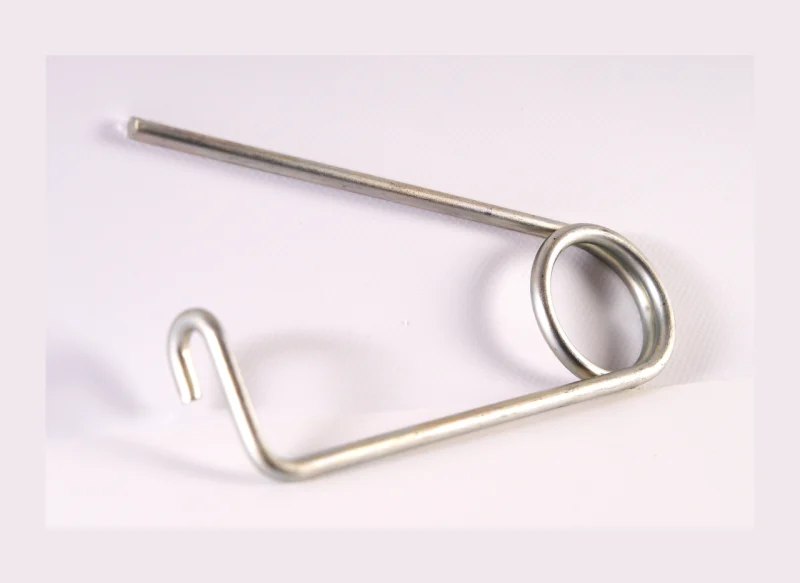 Muelle de torsión de acero de gran calibre sobre fondo blanco, con un cuerpo helicoidal corto de hilo grueso y dos brazos metálicos largos, uno de ellos con una ligera angulación en el extremo.