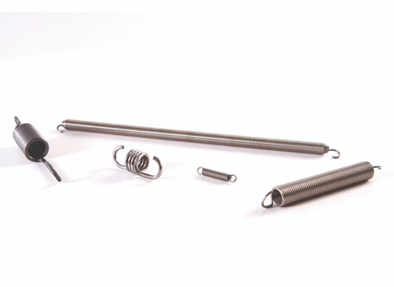 Conjunto de cinco muelles de tracción de diferentes tamaños y longitudes fabricados en acero, con ganchos laterales y ojales en los extremos para fijación mecánica, dispuestos sobre fondo blanco.