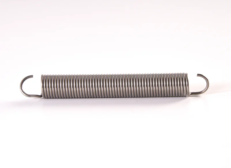 Un muelle de tracción de acero inoxidable dispuesto horizontalmente, con cuerpo cilíndrico de espiras cerradas y ganchos abiertos en ambos extremos sobre fondo blanco.